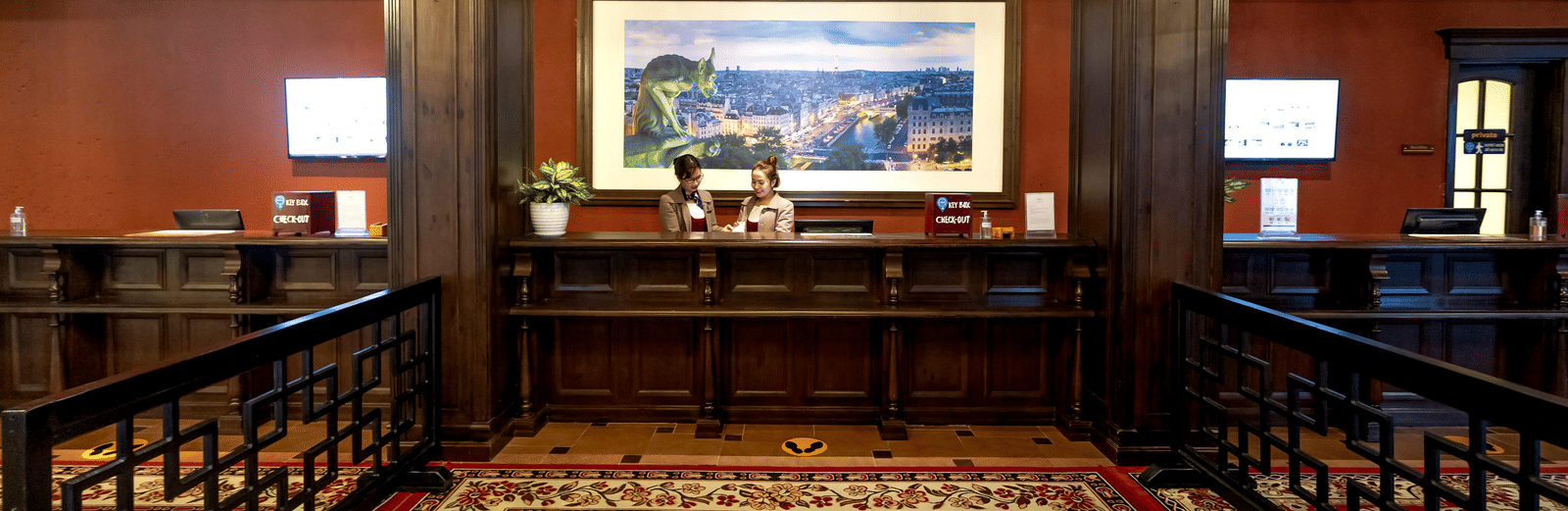 a carpeted front desk lobby with cosy interiors and two staff members standing behind the desk